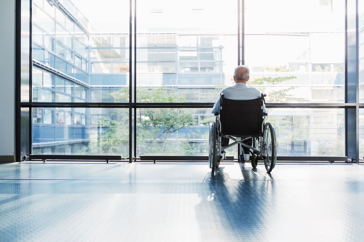 Elderly man in wheelchair faces towards large windows